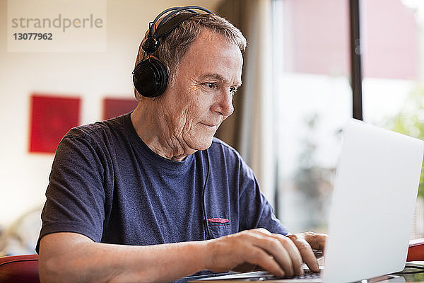 Älterer Mann hört Musik  während er zu Hause einen Laptop benutzt