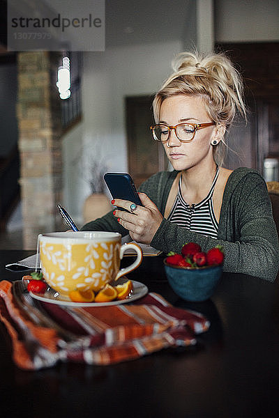Frau benutzt Smartphone  während sie am Frühstückstisch sitzt