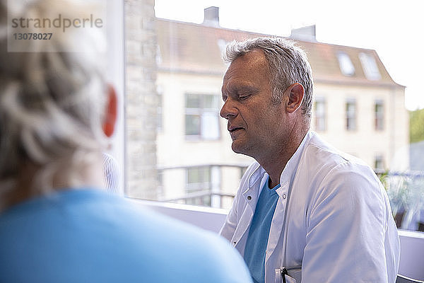 Männlicher Arzt bespricht sich mit einem Kollegen  während er in einer medizinischen Klinik sitzt