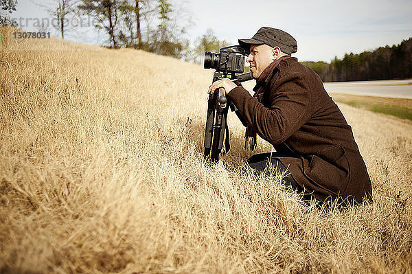 Seitenansicht eines Fotografen mit Stativ  der auf einem Grasfeld kauert