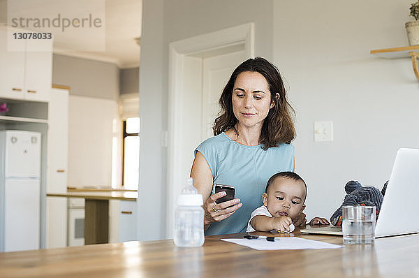 Frau benutzt Smartphone  während sie mit ihrem Sohn zu Hause sitzt