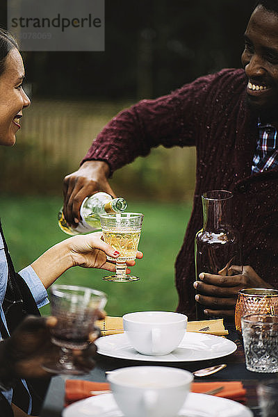 Mann schenkt Wein für einen Freund in einem Glas ein  während er am Tisch sitzt