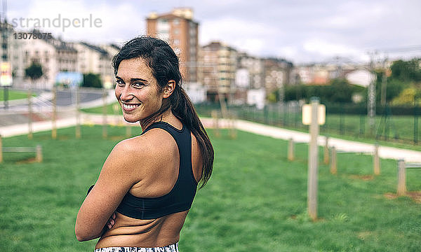 Porträt einer glücklichen Sportlerin  die über die Schulter schaut  während sie im Park steht