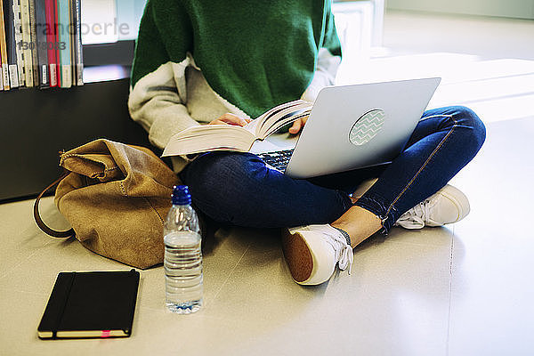 Niedriger Anteil einer Frau  die einen Laptop-Computer benutzt  während sie in der Bibliothek auf dem Boden sitzt