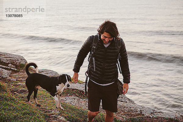 Männlicher Wanderer geht mit Hund auf Felsen am Meer