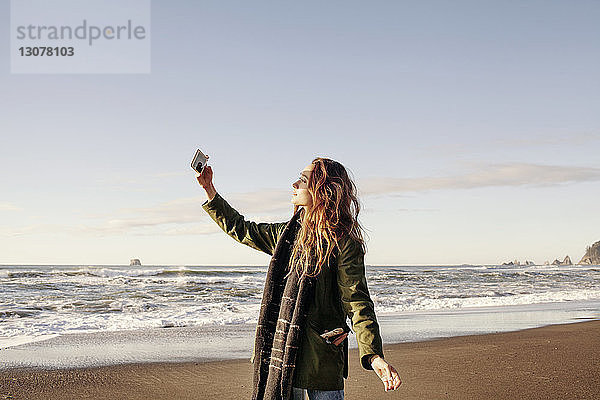 Seitenansicht einer Frau  die mit einem Smartphone am Strand fotografiert