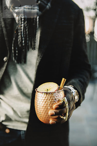 Ein Mann  der im Hinterhof stehend ein Getränk mit einer Apfelscheibe garniert in der Hand hält