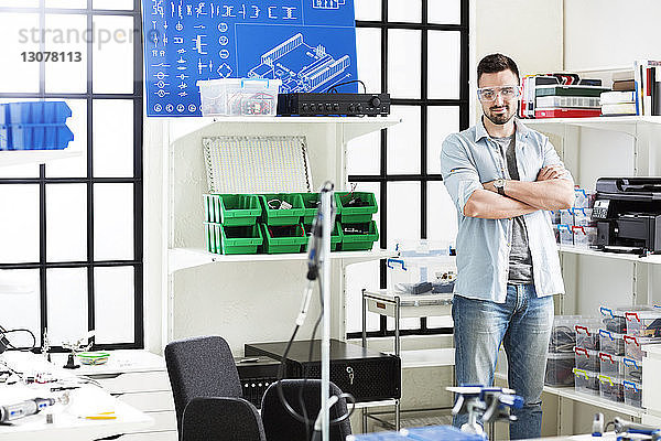 Porträt eines selbstbewussten Ingenieurs  der mit verschränkten Armen im Elektroniklabor steht