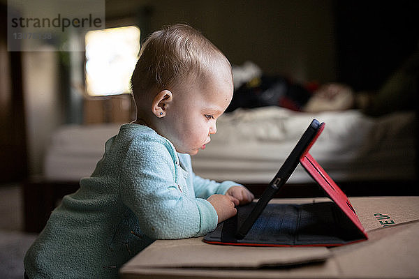 Kleines Mädchen benutzt Tablet-Computer  während es zu Hause an der Kiste steht