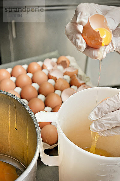 Ausgeschnittenes Bild eines Küchenchefs  der Eier in einem Glas an der Küchentheke zerbricht