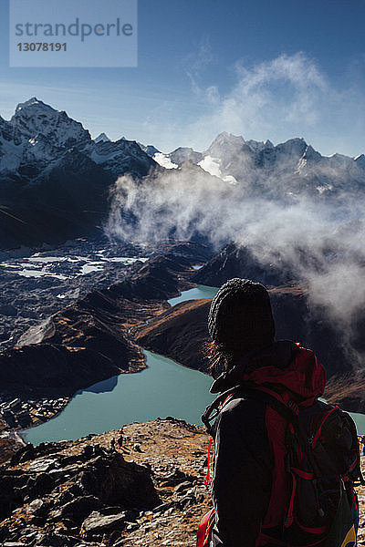 Wanderer mit Rucksack schaut am sonnigen Tag auf Berge vor blauem Himmel