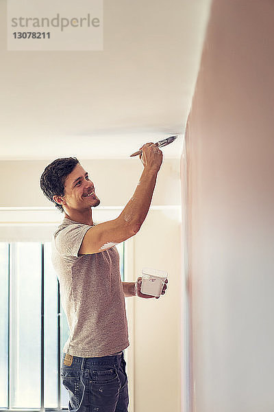 Lächelnder Mann bemalt Wand zu Hause