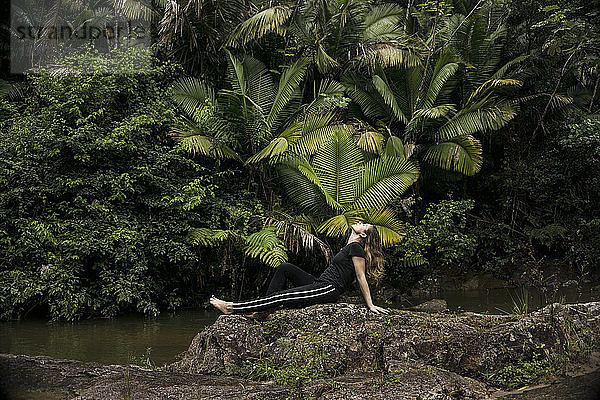 Seitenansicht einer Frau  die sich auf Felsen am Seeufer im El Yunque National Forest entspannt