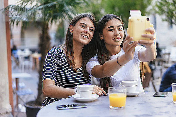 Freunde machen Selbstauslöser mit Sofortbildkamera  während sie im Straßencafé sitzen