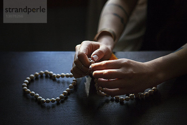 Ausgeschnittenes Bild einer Frau  die mit Perlen in der Dunkelkammer zu Hause betet