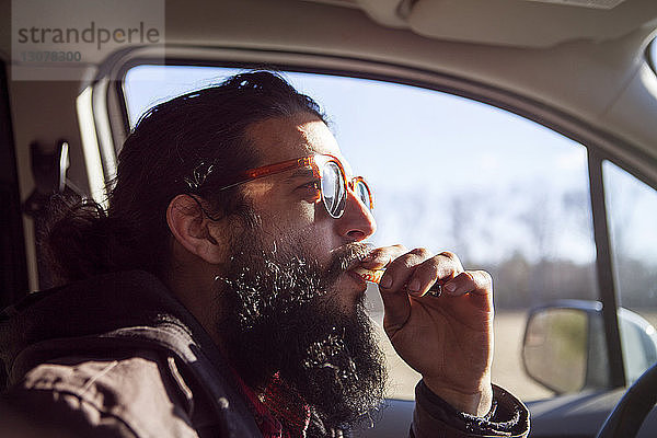 Seitenansicht eines männlichen Hipsters  der eine elektronische Zigarette im Auto raucht