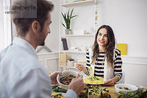 Glückliche Frau isst Spaghetti-Nudeln  während sie einen Freund beim Mittagessen anschaut