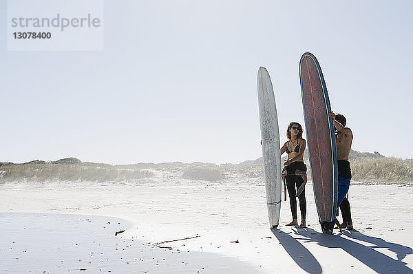 Freunde mit Surfbrettern stehen am Strand vor klarem Himmel an einem sonnigen Tag