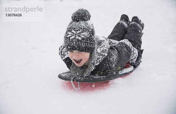 Fröhlicher Junge schlittert bei Schneefall auf Schnee