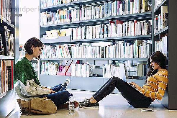 Freundinnen  die mit Laptop-Computern lernen  während sie in der Bibliothek auf dem Boden sitzen
