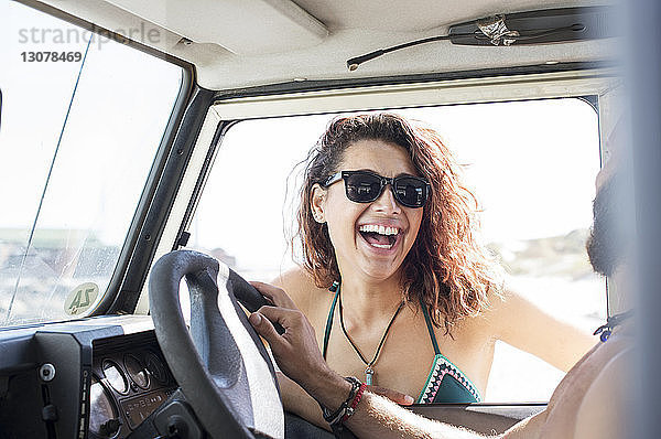 Fröhliche Frau mit Sonnenbrille im Gespräch mit einem Freund  der im Geländewagen sitzt