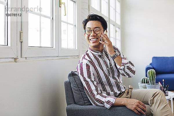 Glücklicher Geschäftsmann spricht am Smartphone  während er im Büro durchs Fenster schaut
