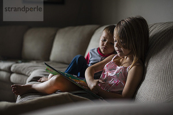 Geschwister schauen Bilderbuch auf dem Sofa an