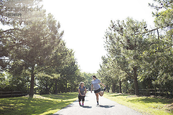 Mutter und Tochter strecken die Beine  während sie sich bei Sonnenschein auf einem Fußweg im Park bewegen
