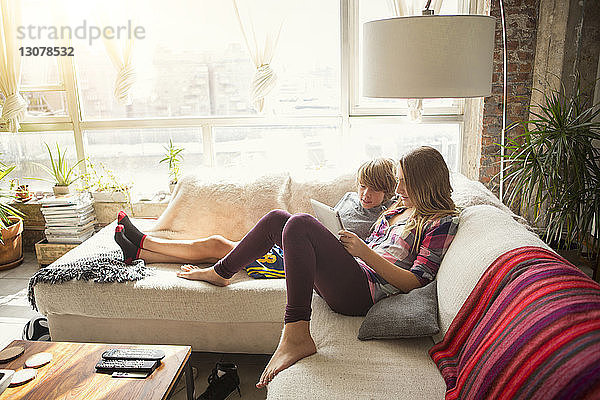 Kinder schauen auf Tablet-Computer  während sie auf dem Sofa im Wohnzimmer sitzen