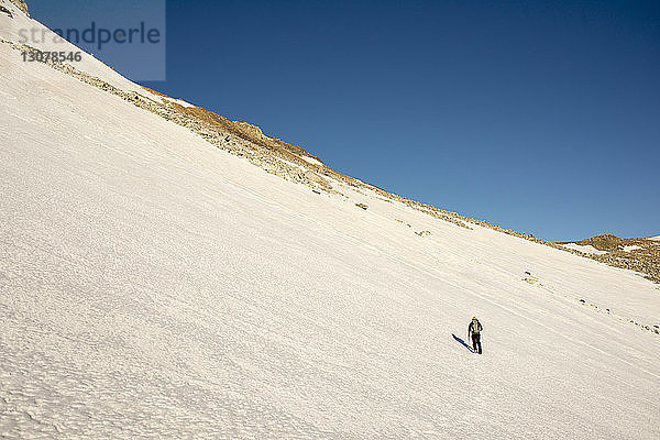 Rückansicht eines Mannes  der auf einem verschneiten Feld vor strahlend blauem Himmel wandert