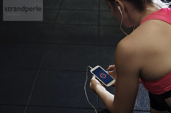 Hochwinkelansicht einer Sportlerin  die ein Smartphone im Fitnessstudio benutzt