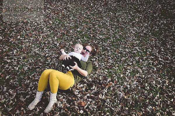 Hochwinkelaufnahme einer Frau mit einem kleinen Mädchen  das auf trockenen Blättern auf dem Feld liegt
