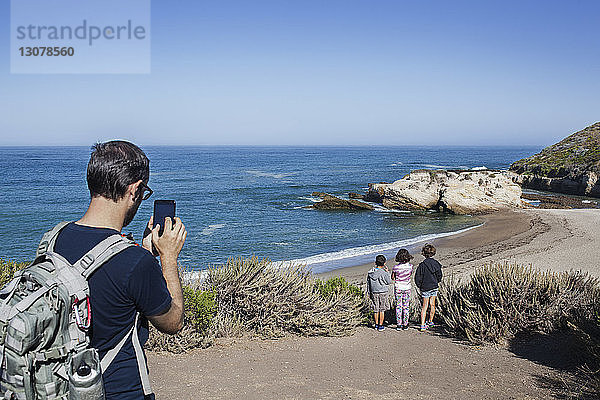 Vater fotografiert Kinder am Strand gegen den Himmel