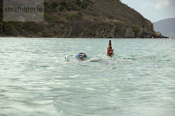 Mann hält Bierflasche beim Schwimmen im Meer