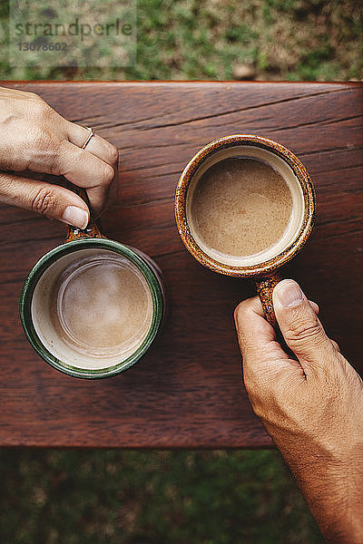 Geschorene Hände eines Paares  das Kaffeetassen am Geländer hält