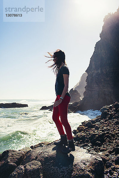 Frau steht auf Fels am Ufer gegen Meer und Himmel am sonnigen Tag