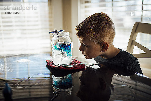 Junge schaut in Glas auf den Tisch  während er zu Hause sitzt