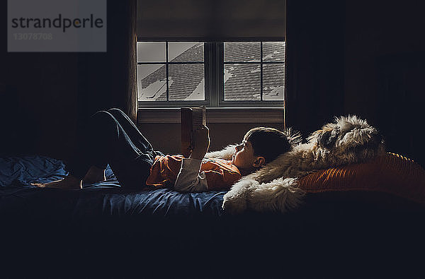 Seitenansicht eines Jungen  der zu Hause auf dem Bett liegt und ein Buch liest