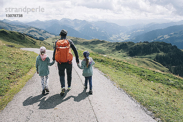 Rückansicht einer Mutter mit Töchtern  die auf einer Bergstraße gegen bewölkten Himmel gehen