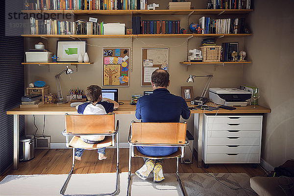Rückansicht von Vater und Sohn am Laptop zu Hause
