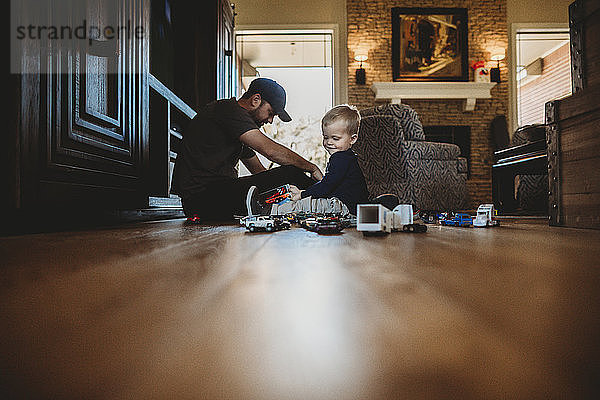 Ebenerdiges Bild von Vater und Sohn  die zu Hause mit Spielzeugautos auf dem Boden spielen