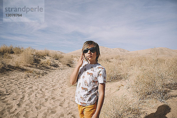 Junge mit Sonnenbrille  der an einem sonnigen Tag in der Wüste steht