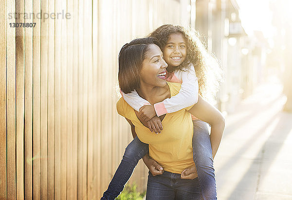Glückliche Mutter nimmt ihre Tochter bei Sonnenschein huckepack