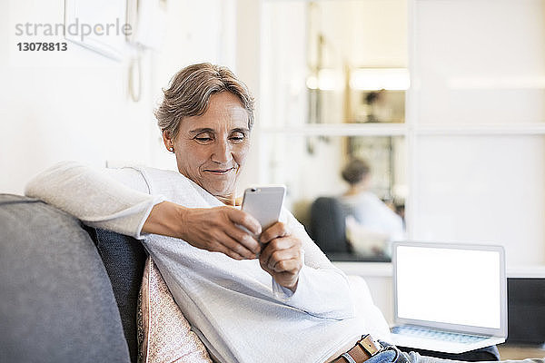 Reife Frau benutzt Smartphone  während sie zu Hause auf dem Sofa sitzt