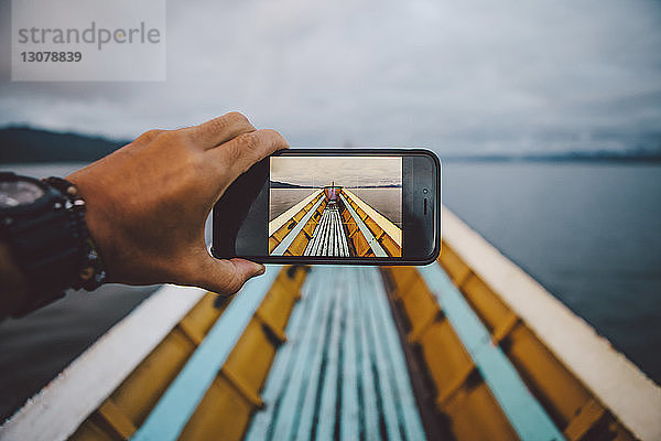 Abgetrennte Hand eines Mannes fotografiert Boot durch Smartphone gegen den Himmel