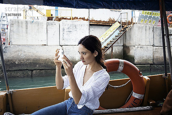 Weibliche Touristin fotografiert im Boot sitzend per Smartphone