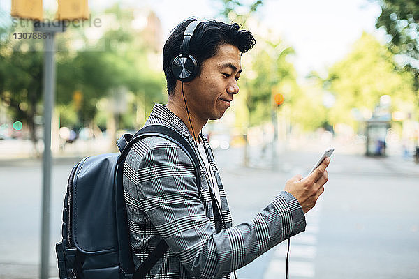 Geschäftsmann mit Rucksack benutzt Smartphone  während er auf einem Fußweg Musik hört