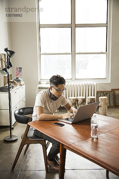 Geschäftsmann mit Kopfhörer und Laptop am Tisch im Kreativbüro