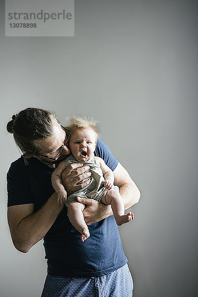 Vater trägt gähnende Tochter  während er vor grauem Hintergrund steht