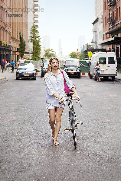 Frau zu Fuß mit Fahrrad auf der Straße in der Stadt